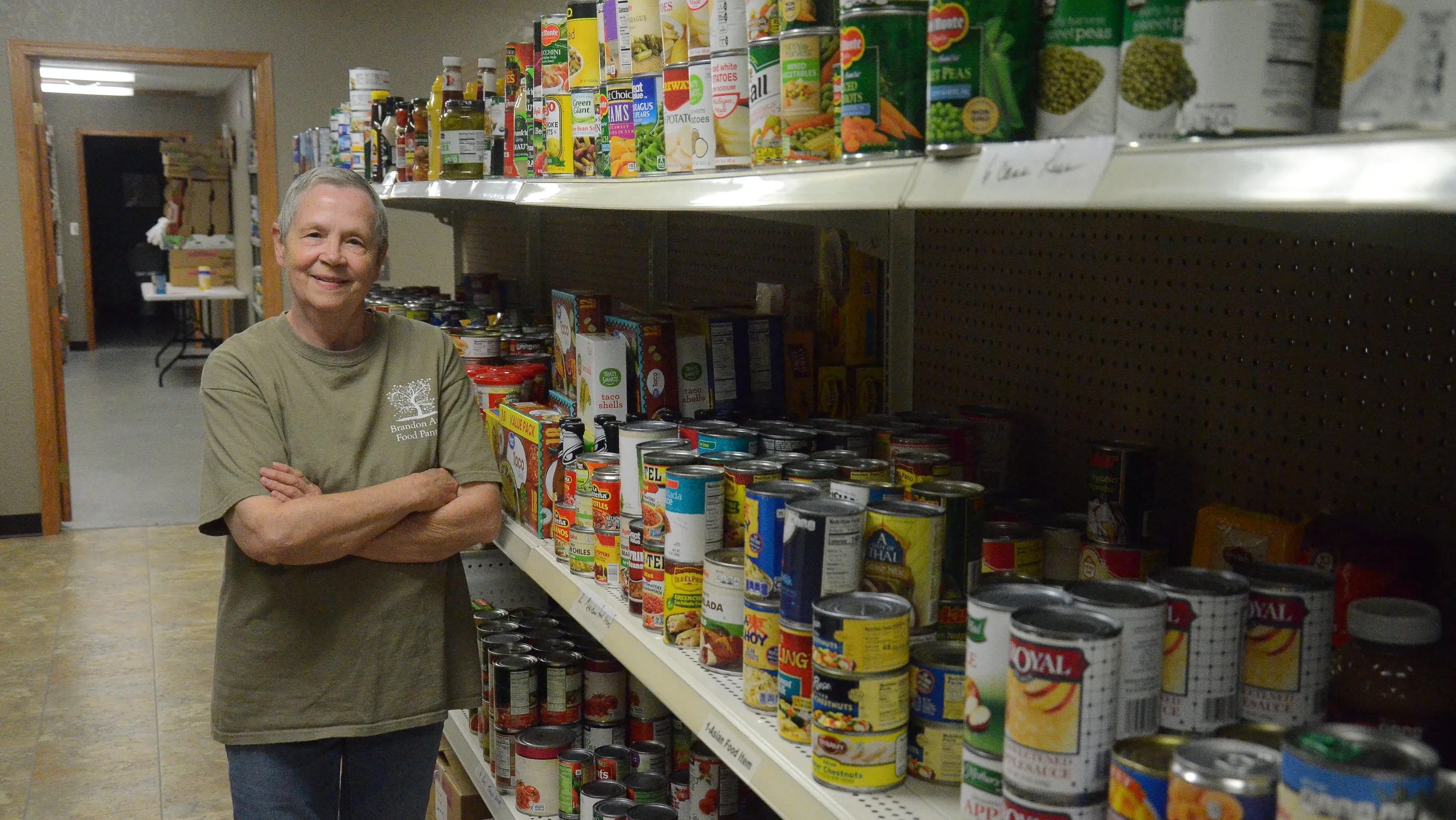 Volunteer standing next to food pantry shelves stocked with goods